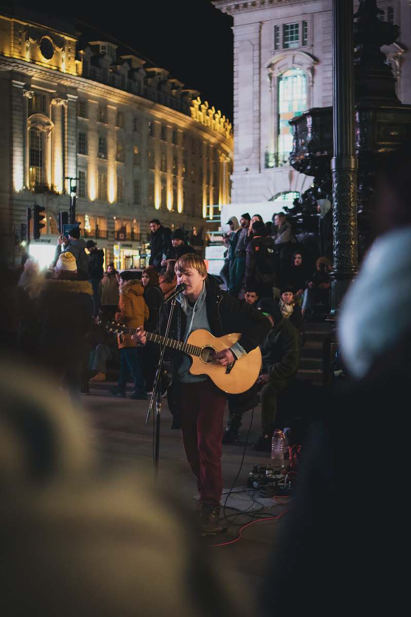 guitar man in black t-shirt playing guitar on street during night time leisure activities